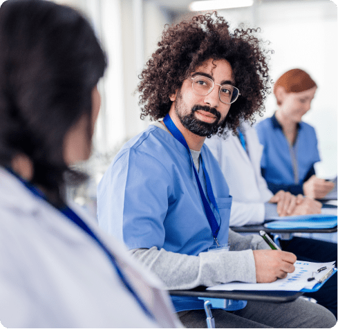 Group of healthcare professionals in scrubs sitting and chatting, engaging in a discussion or teamwork in a medical setting.