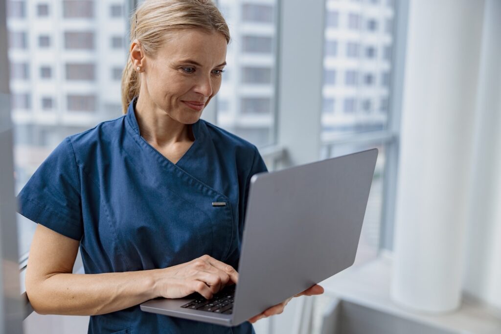 Female healthcare worker using laptop to manage hospital healthcare software and patient flow management in a hospital setting